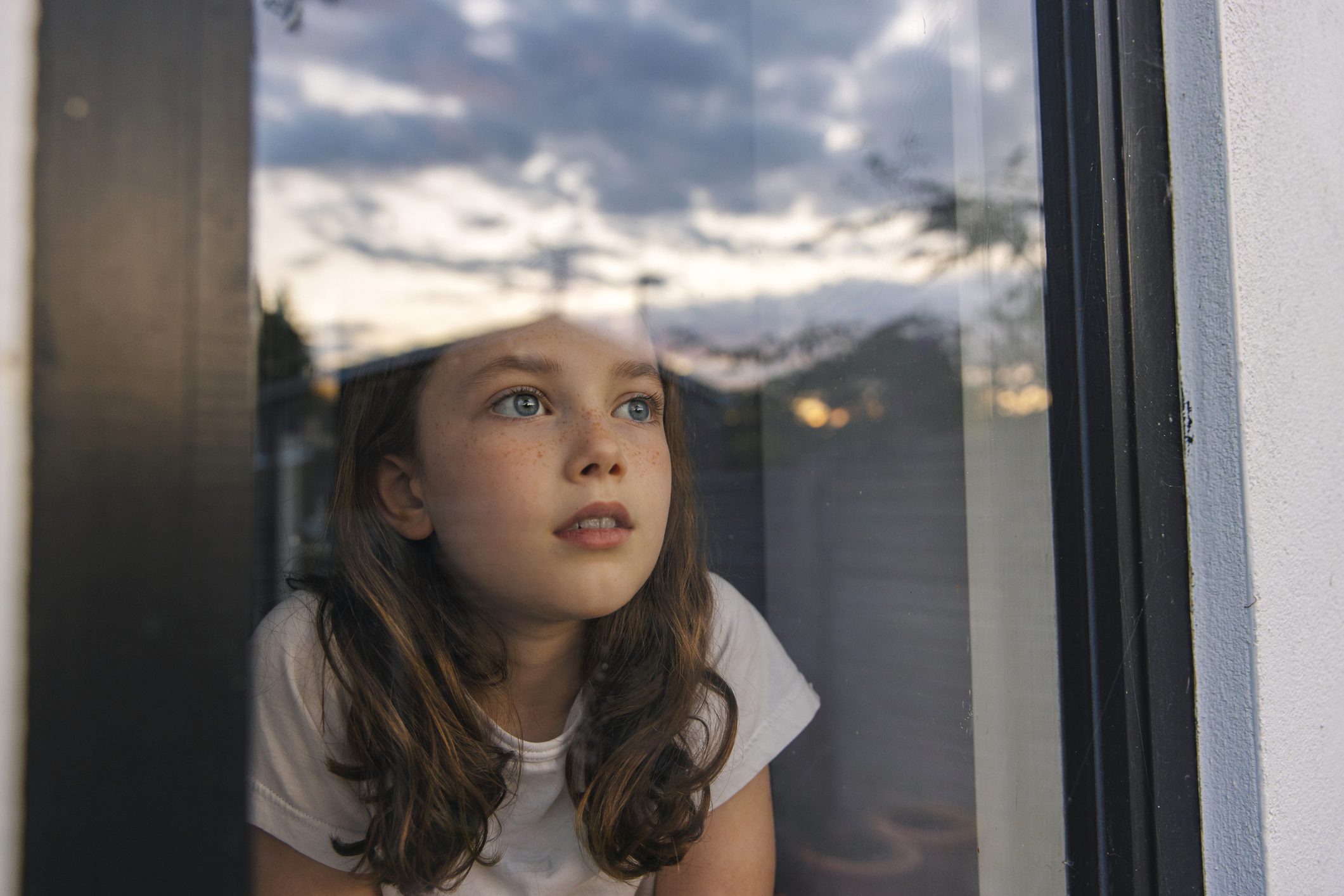 Young girl gazes hopefully out of her bedroom window.