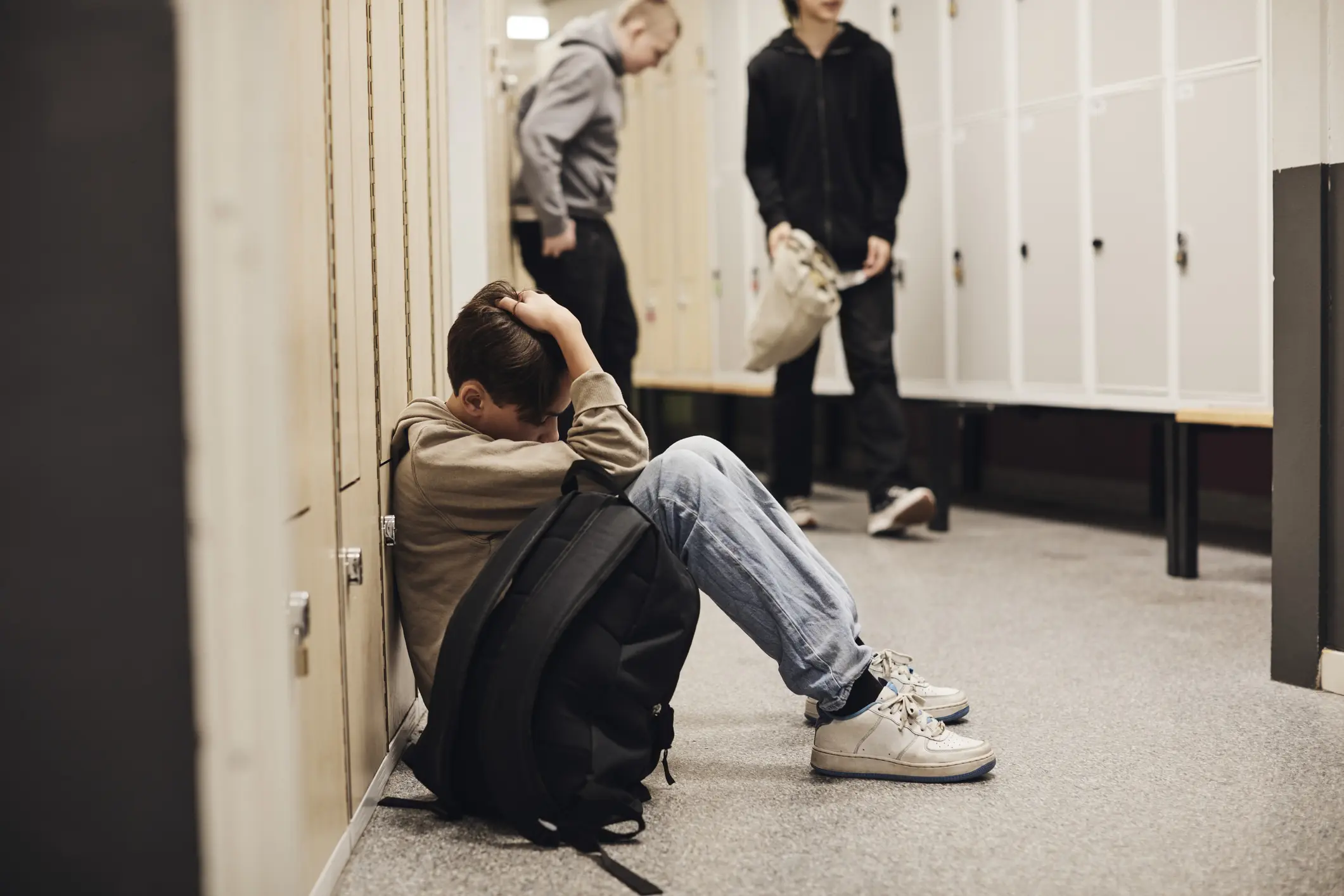 Depressed teen holds his head in his hands as he sits on the floor leaning against his locker in school.